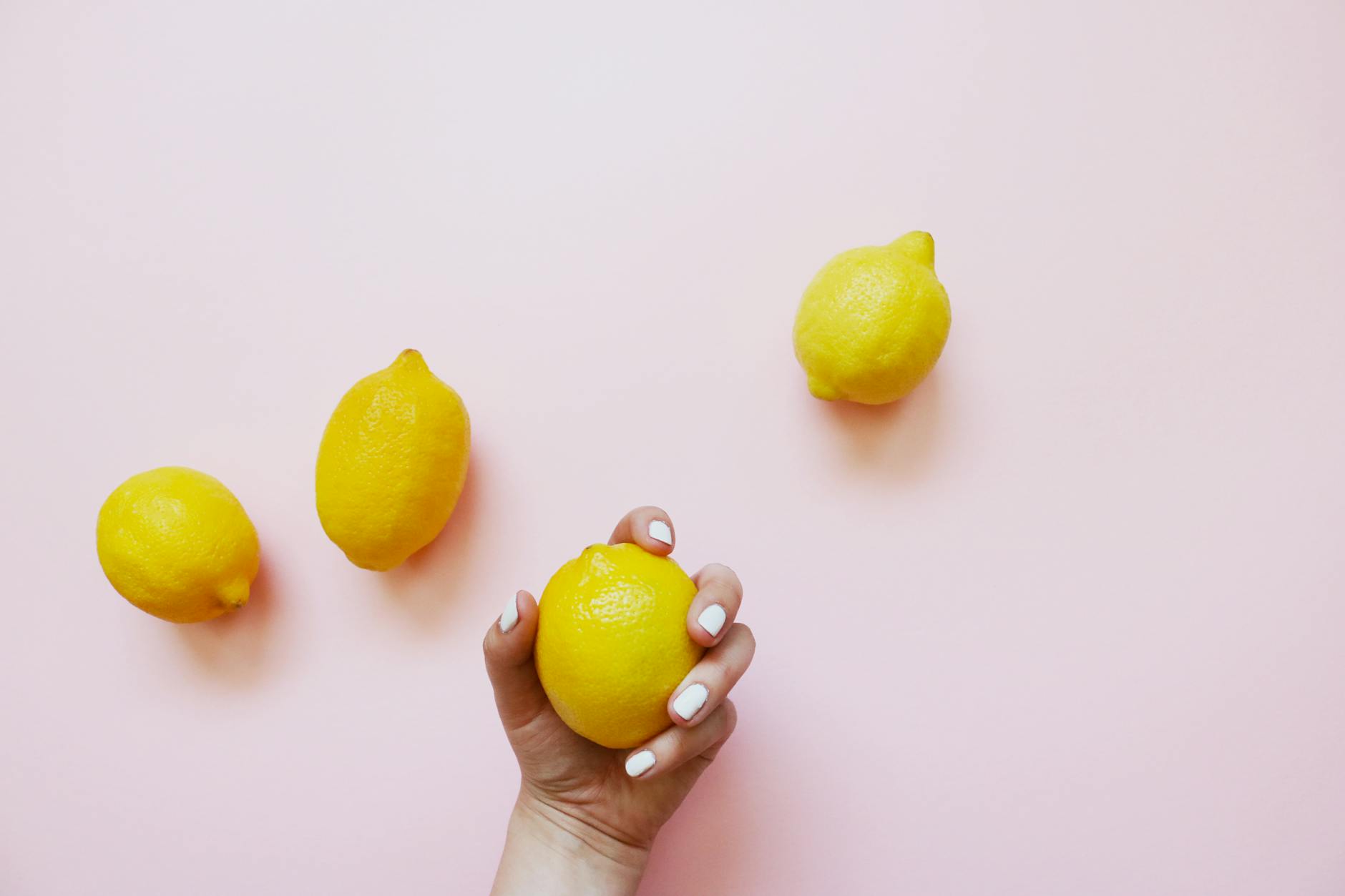 A hand holding a lemon on a soft pink background, symbolizing gentle recovery and renewed sensation