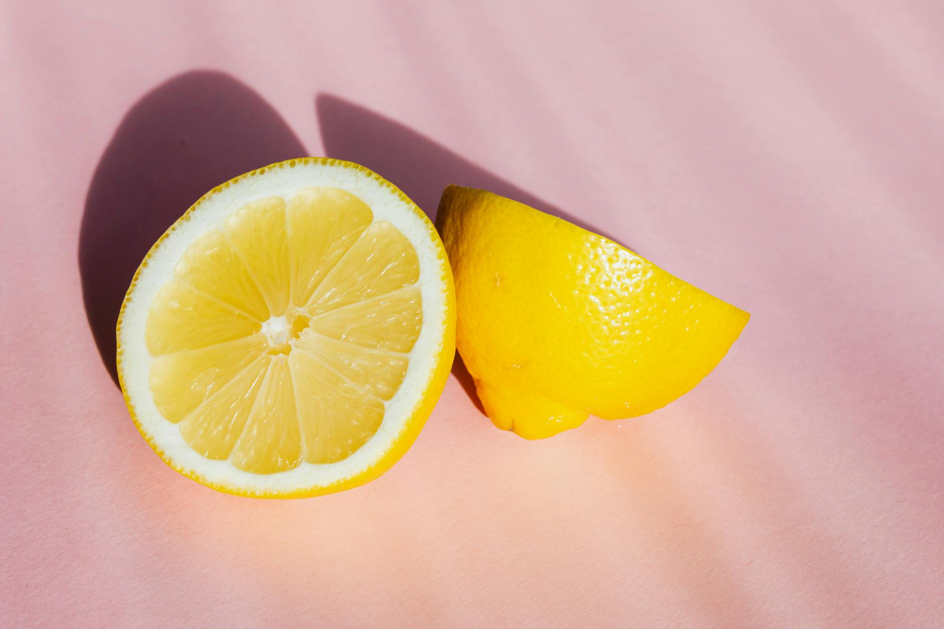Fresh lemon halves on a pink background in sunlight, symbolizing the bright clarity of ovulation and heightened sensation