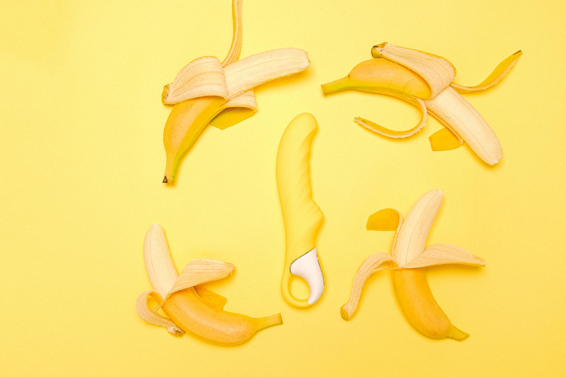 A sleek lemon vibrator surrounded by fresh lemons on a bright yellow background.