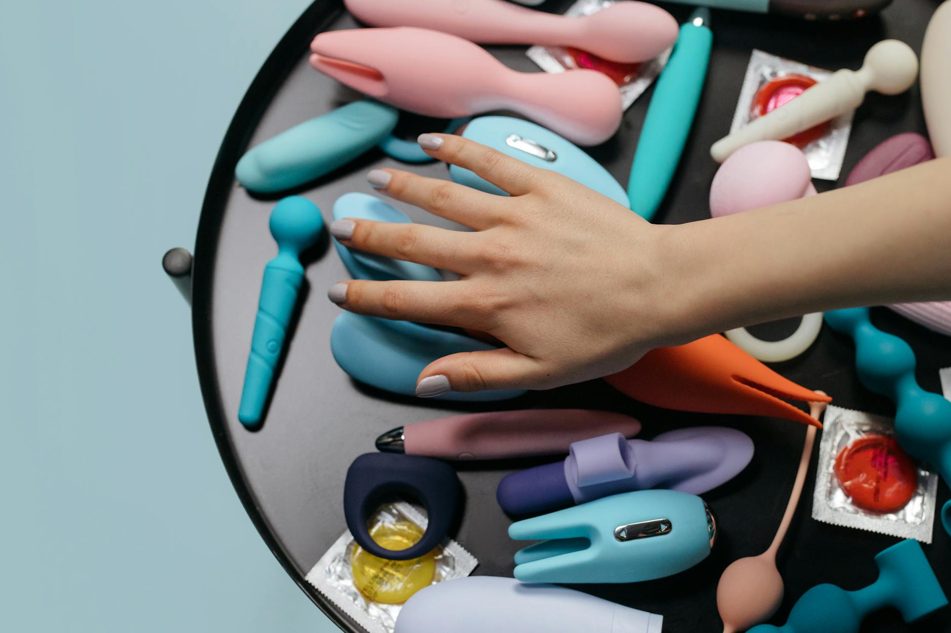 Close-up of a woman holding a pink vibrator, with art books in the background, emphasizing intimate self-care and personal pleasure.