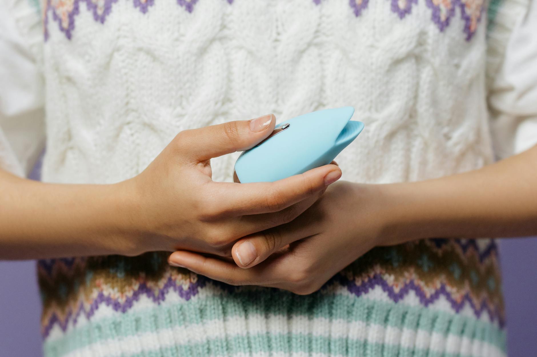 Blue silicone vibrator held in hand against purple background for intimate self-pleasure