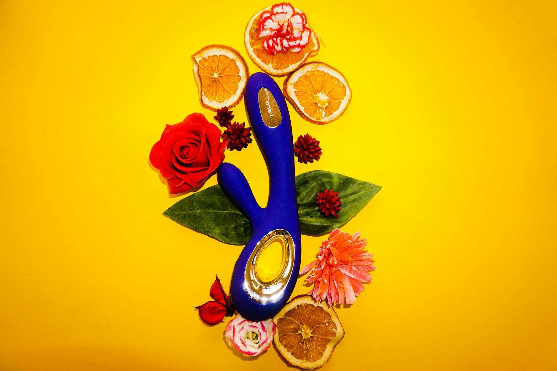 Un vibromasseur citron entouré de fleurs et de tranches d'orange sur fond jaune
