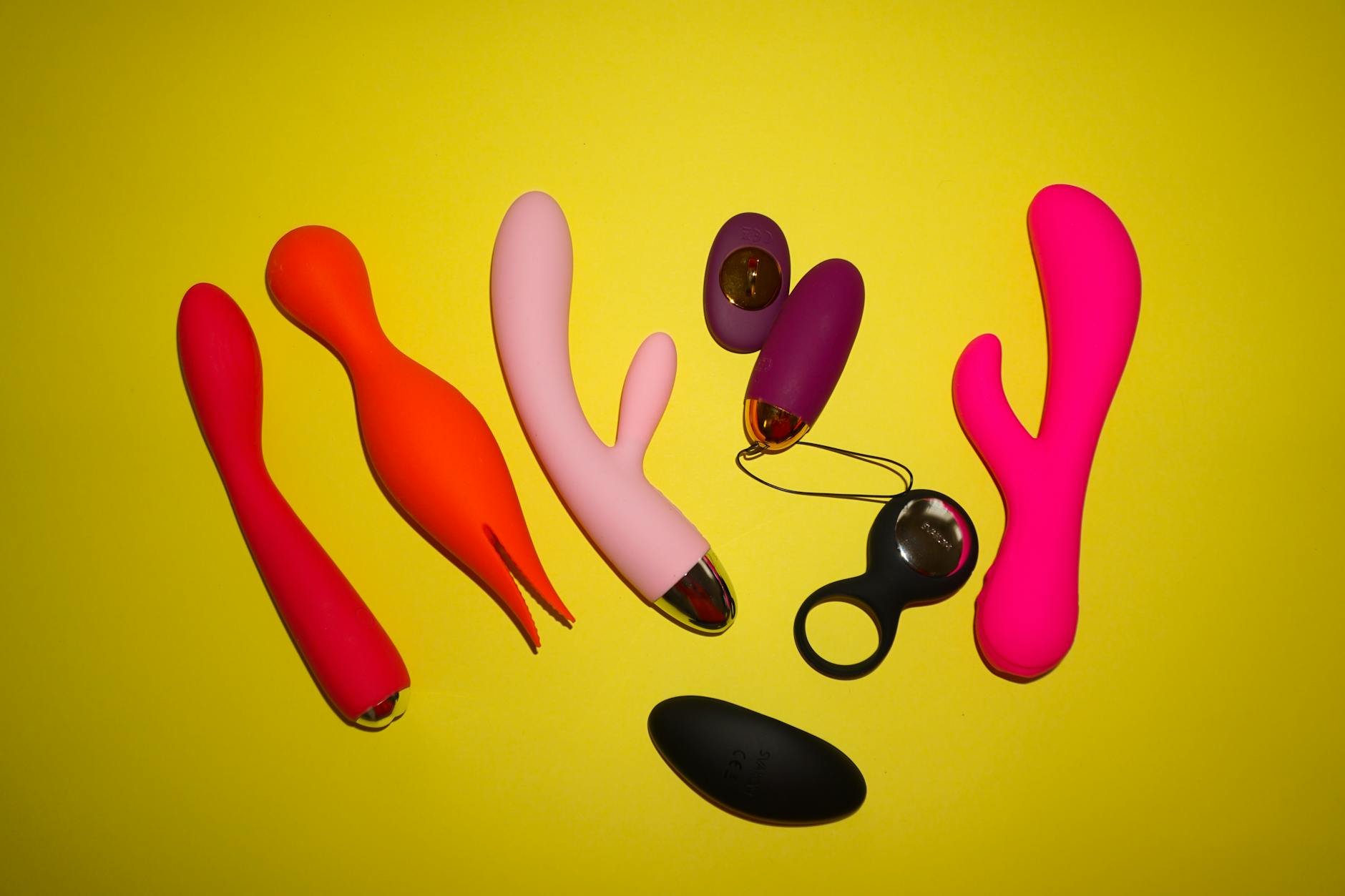 Hands holding pink and blue silicone clitoral vibrators against a pastel background